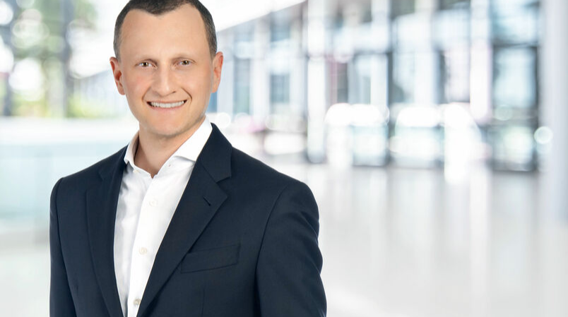 Portrait of a smiling businessman in a dark blue suit and white shirt in a modern office environment.